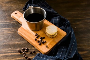 Antika bir fincanda İtalyan amerikan kahvesi, kahve çekirdekleri, şekerli el yapımı kurabiye ve arkasında da bir moka demliği. Her şey eski ahşap arka planda ve sağlıklı ve lezzetli bir kahvaltı..