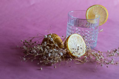 Alkol içeceği (cin ve tonik kokteyl) limon meyvesi ve pembe arka planda izole edilmiş çiçek ile süslenmiştir. Limonlu ve otlu buzlu kokteyl..