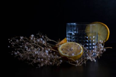 Alkol içeceği (cin ve tonik kokteyl) limon meyvesi ve siyah arka planda izole edilmiş çiçek ile süslenmiştir. Limonlu ve otlu buzlu kokteyl..
