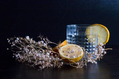 Alkol içeceği (cin ve tonik kokteyl) limon meyvesi ve siyah arka planda izole edilmiş çiçek ile süslenmiştir. Limonlu ve otlu buzlu kokteyl..