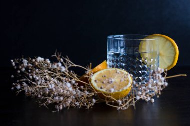 Alkol içeceği (cin ve tonik kokteyl) limon meyvesi ve siyah arka planda izole edilmiş çiçek ile süslenmiştir. Limonlu ve otlu buzlu kokteyl..