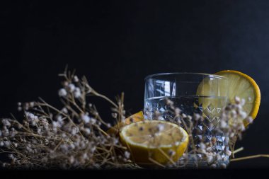 Alkol içeceği (cin ve tonik kokteyl) limon meyvesi ve siyah arka planda izole edilmiş çiçek ile süslenmiştir. Limonlu ve otlu buzlu kokteyl..