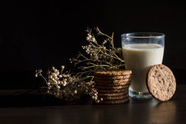 Sağlıklı bir sabah kahvaltısı, bardakta taze süt ve klasik koyu arkaplanda ev yapımı çikolatalı kurabiye. Yiyecek ve Çiçekler Estetik bileşimi.