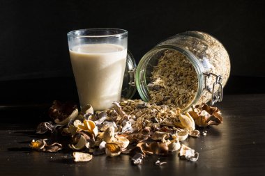 Sabah mısır gevreği, tam tahıl ve sütle servis edilen sağlıklı bir kahvaltı. Kalın bir bardakta, eski tarz, ahşap arka planda. Çiçekler ve besin estetiği.