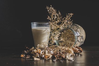 Sabah mısır gevreği, tam tahıl ve sütle servis edilen sağlıklı bir kahvaltı. Kalın bir bardakta, eski tarz, ahşap arka planda. Çiçekler ve besin estetiği.