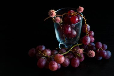 Red grapes, large bunch of fruits, fresh and tasty simple food with bright colors on a black background. flowers and fruit for an artistic food composition.