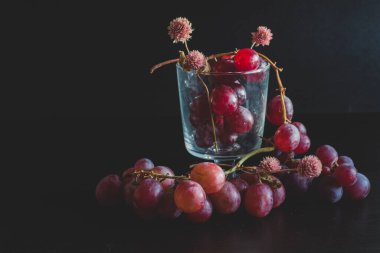 Red grapes, large bunch of fruits, fresh and tasty simple food with bright colors on a black background. flowers and fruit for an artistic food composition.