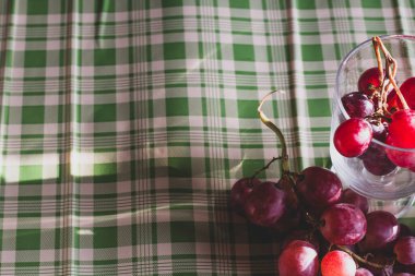 Red grapes, large bunch of fruits, fresh and tasty simple food with brights red and violet colors on a green background in an amazing composition