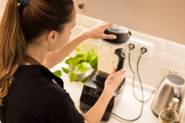 Genç ve çekici bir kadın mutfakta mikserin önünde duruyor ve aileye taze vejetaryen yemekleri pişiriyor. Genç sarışın kadın mutfakta taze sebze pişiriyor.