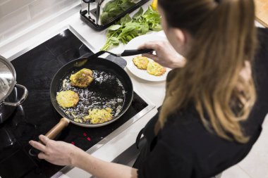 Genç, çekici İsveçli kadın mutfağında yemek pişiriyor ve ailesi için sağlıklı Akdeniz yemekleri hazırlıyor. Genç yemek blogcusu mutfağında yemek hazırlıyor, sebze kızartıyor.