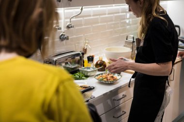 Genç, çekici İsveçli kadın mutfağında yemek pişiriyor ve ailesi için sağlıklı Akdeniz yemekleri hazırlıyor. Genç yemek blogcusu mutfağında yemek hazırlıyor, sebze kızartıyor.