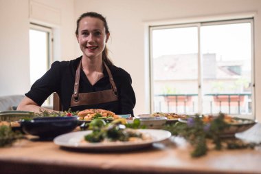 Genç ve çekici İsveçli yemek blogcusu yemek tabaklarının önünde poz veriyor. Tahta bir masanın önünde oturan genç bir kız vejetaryen yemekleri ve sağlıklı bulaşıkları yiyor. Vejetaryen yaşam tarzı