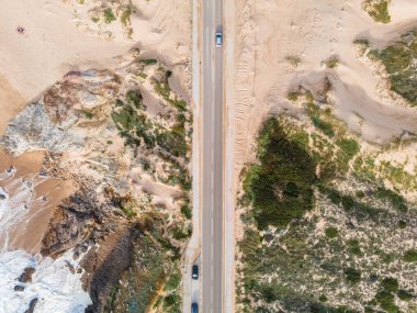Atlantik Okyanusu 'na bakan vahşi güney kıyı şeridi boyunca giden araçların bulunduğu dar bir yolun hava manzarası kayalıklarda, Cascais, Portekiz.