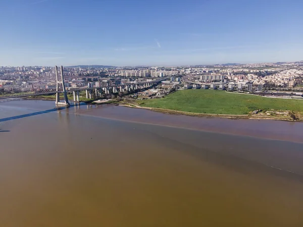 Aerial view of a garden park facing the Tagus river next the Vasco da Gama bridge with Trancao river and Lisbon residential district skyline in background, Portugal.