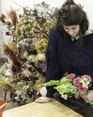 Çiçekçi olarak çalışan genç bir kadının çiçekçide bir buket güzel çiçek düzenlemesi..