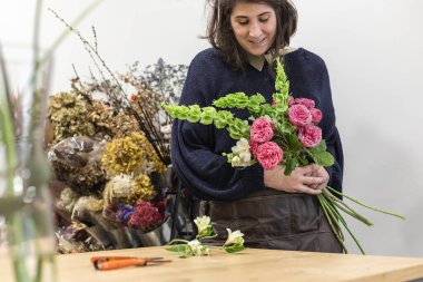 Çiçekçi olarak çalışan genç bir kadının çiçekçide bir buket güzel çiçek düzenlemesi..