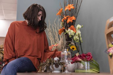 Çiçekçisindeki ahşap masada oturan neşeli bir çiçekçinin portresi. Genç iş kadını konsepti.