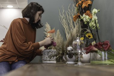 Çiçekçi dükkanında çalışan genç bir kadının ahşap masada oturup çiçek dekorasyonu ve iş kadını konsepti yaratması..