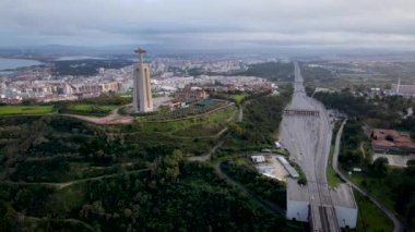 Aerial drone view flyby past Sanctuary of Christ the King Portuguese Santuario de Cristo Rei is Catholic monument next to the 25 de April bridge overlooking city of Lisbon Almada