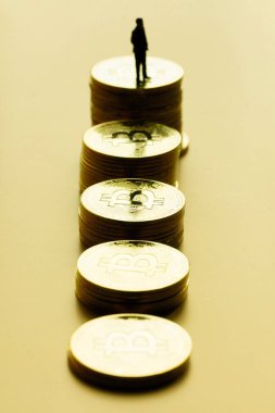 Altın zemin üzerinde işadamı minyatürü olan bitcoin yığınlarının görüntüsü. Bitcoin yükseltme pazarının dikey görüntüsü.