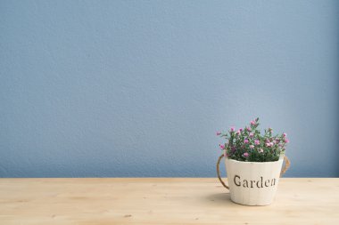 Wood table with pink rose on flower pot and  blue cement wall.
