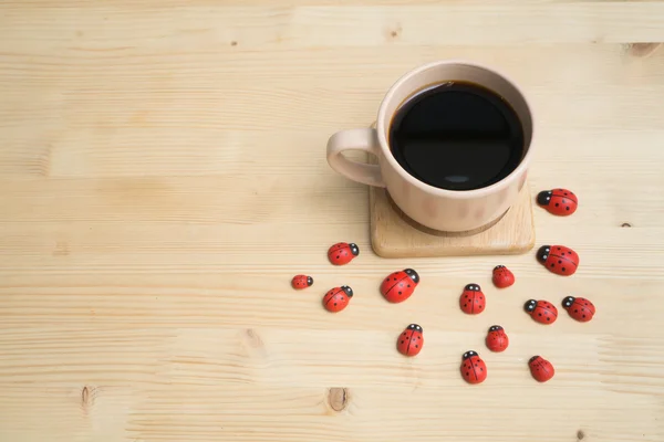 Дерев'яний обідній стіл з чорною кавою та червоним сонечком  . — стокове фото