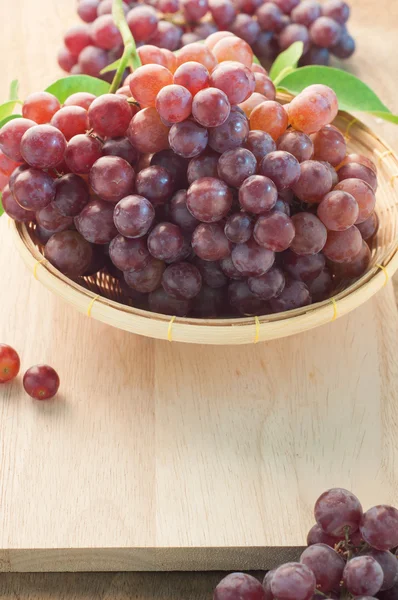 Uvas en una cesta de bambú y tablas de cortar de madera . —  Fotos de Stock