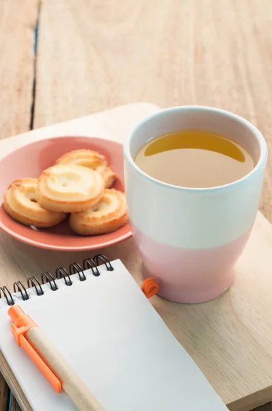 Taza de té, galletas de postre en papel madera piso y Bloc de notas. — Foto de Stock