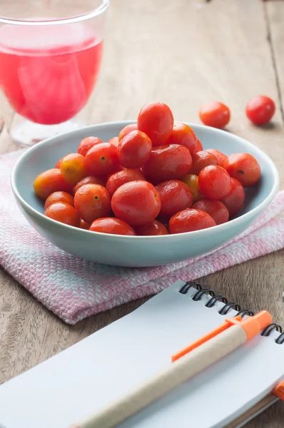 Small tomato on the palette  And tomato juice in a glass. — Stock Photo, Image