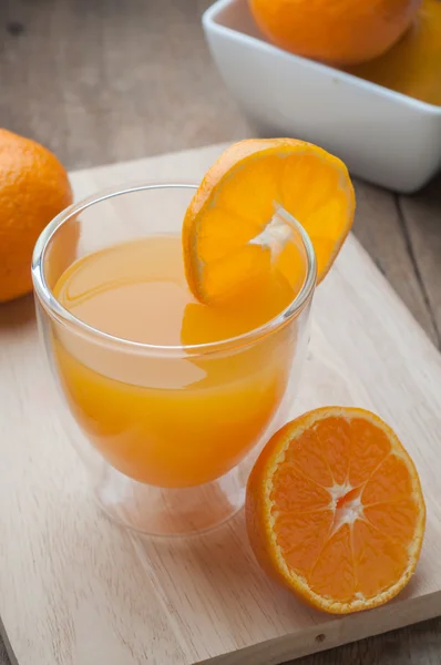 Bicchiere di succo d'arancia su un tagliere di legno e pavimenti in legno . — Foto Stock