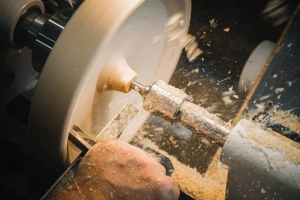 a man in a working apron works on a wood turning lathe. hands hold a chisel. hobby