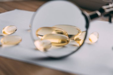 Büyüteç altında sarı şeffaf omega 3 kapsülleri. vitamin geliştirme kavramı