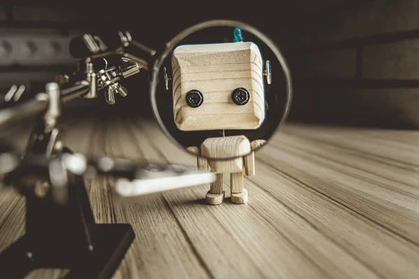 Ahşap robot android büyüteç altındaki bir masanın üzerinde duruyor. Büyüteçle metal kıskaçlar. Güzelleştirici bardaktaki bir robotun yüzü. İnsan eğitim konsepti