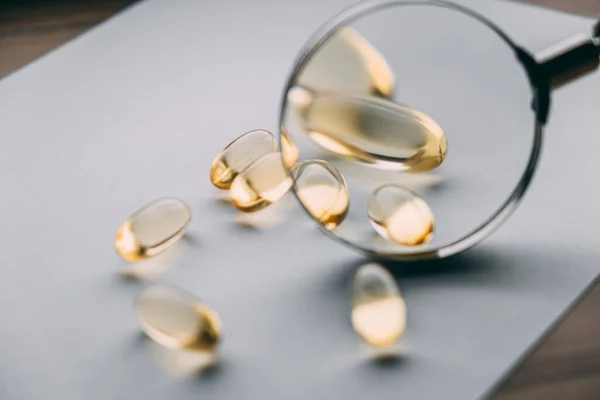 Büyüteç altında sarı şeffaf omega 3 kapsülleri. vitamin geliştirme kavramı