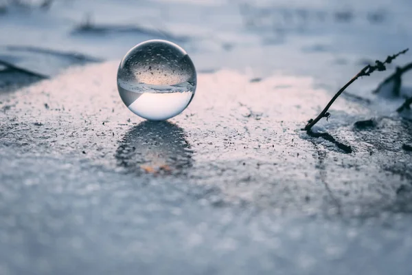 glass transparent ball on an ice crust in winter, reflected on ice. dawn