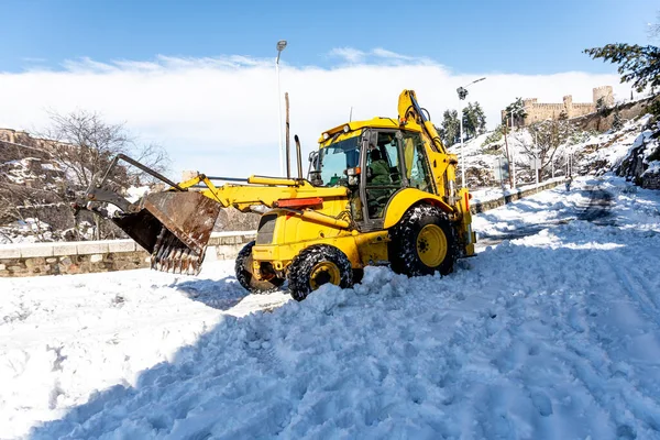 Yellow excavator removing snow in the city.