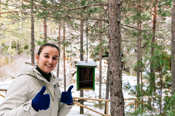 Happy woman because she just placed a wooden bird nest in the forest. Snowy landscape