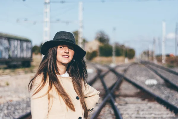 Happy woman in beige raincoat and hat on abandoned railroad tracks.