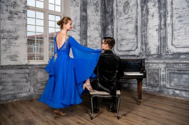 Genç adam, gri dans salonunda mavi balo elbiseli bir kızla dans ediyor.