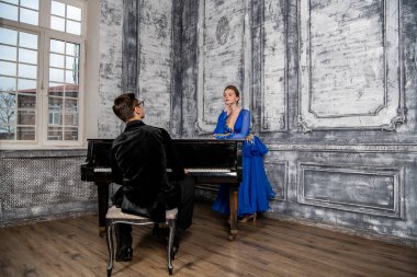 Genç adam, gri dans salonunda mavi balo elbiseli bir kızla dans ediyor.