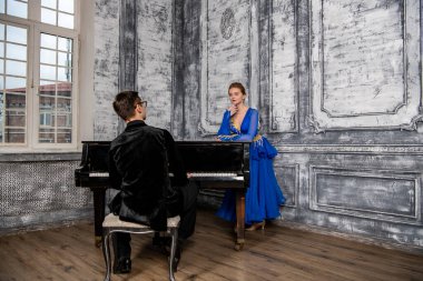 Genç adam, gri dans salonunda mavi balo elbiseli bir kızla dans ediyor.