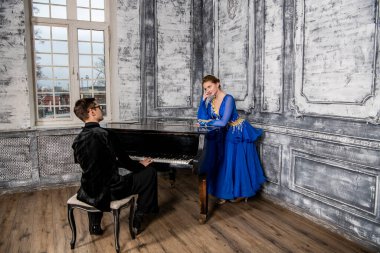 Genç adam, gri dans salonunda mavi balo elbiseli bir kızla dans ediyor.