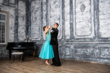 Siyah takım elbiseli genç bir adam dans salonunda turkuaz elbiseli bir kızla dans ediyor.