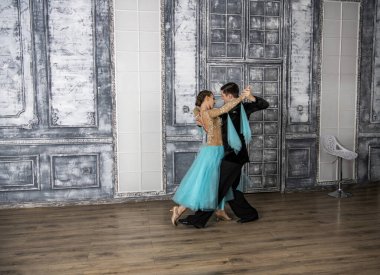 Siyah takım elbiseli genç bir adam dans salonunda turkuaz elbiseli bir kızla dans ediyor.