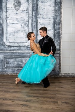 Siyah takım elbiseli genç bir adam dans salonunda turkuaz elbiseli bir kızla dans ediyor.