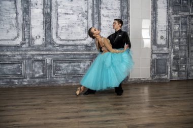 Siyah takım elbiseli genç bir adam dans salonunda turkuaz elbiseli bir kızla dans ediyor.