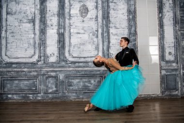 Siyah takım elbiseli genç bir adam dans salonunda turkuaz elbiseli bir kızla dans ediyor.