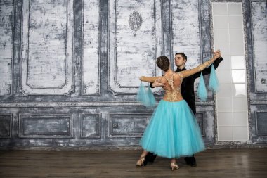 Siyah takım elbiseli genç bir adam dans salonunda turkuaz elbiseli bir kızla dans ediyor.