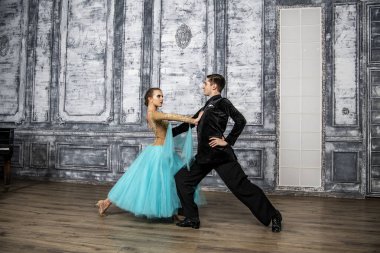 Siyah takım elbiseli genç bir adam dans salonunda turkuaz elbiseli bir kızla dans ediyor.