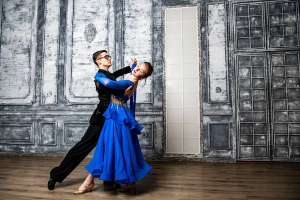 young man dancing with a girl in a blue ballroom dress in a gray dance hall